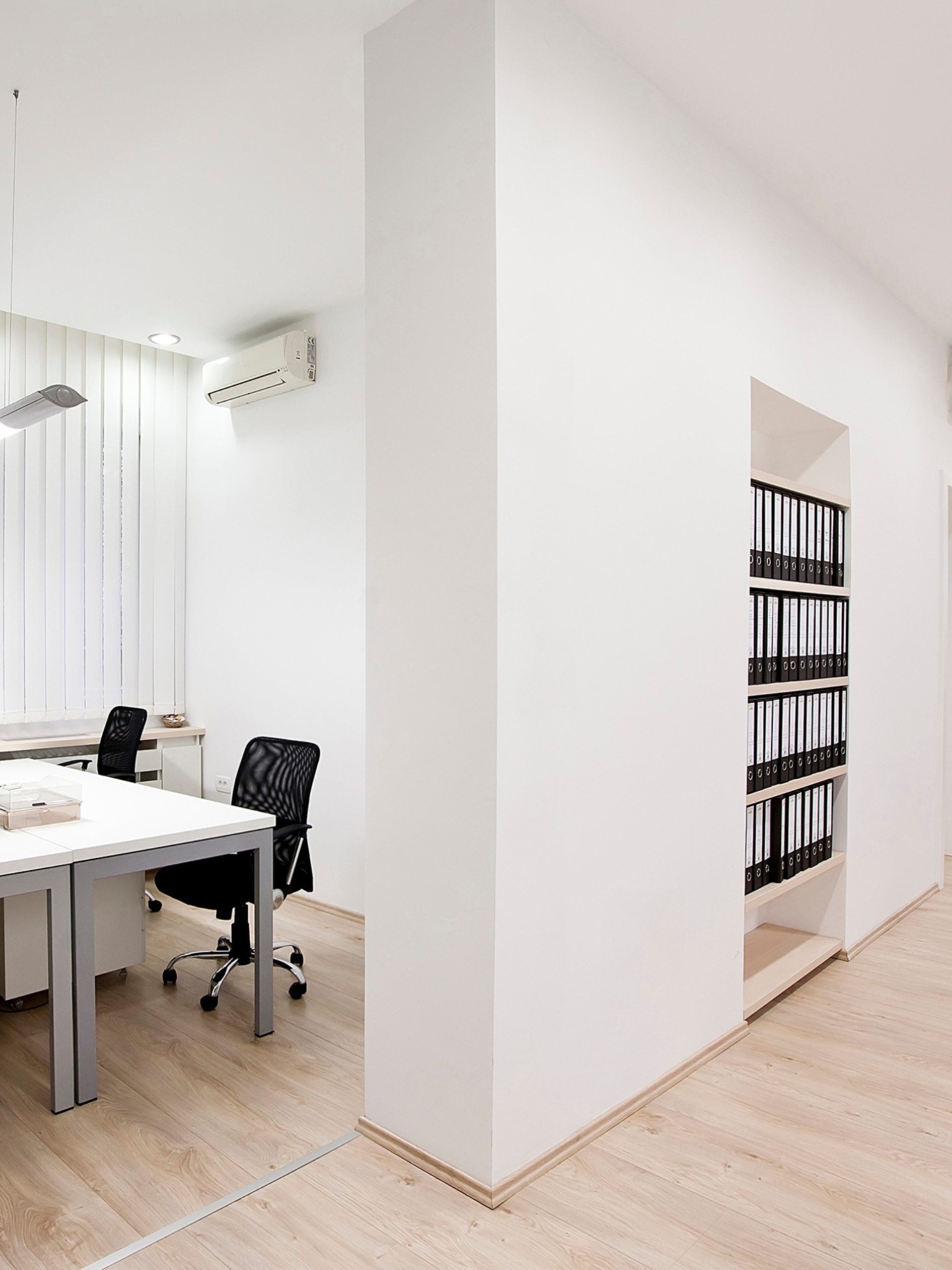 Orange Coworking Built to Suit 3 Sala privativa iluminada no Orange Coworking com mesas brancas, cadeiras pretas ergonômicas e estante embutida com pastas organizadoras.