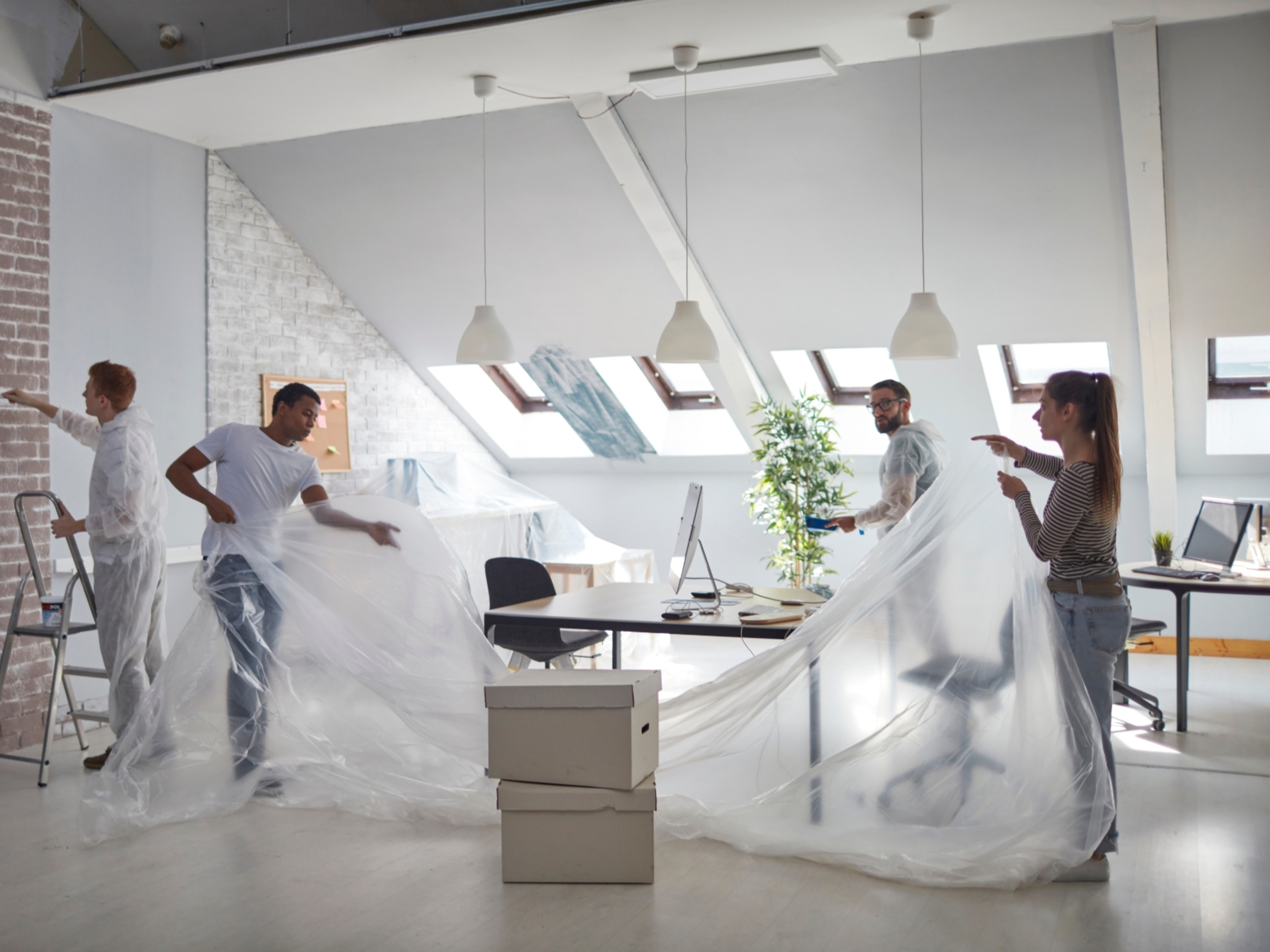 Orange Coworking Built to Suit 4 Processo de reforma e expansão no Orange Coworking. Pessoas cobrindo as estações de trabalho com lona plástica e pintando parede ao fundo.